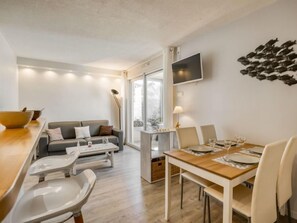 Una sala de estar moderna con sofá, mesa de comedor y sillas. Hay un televisor montado en la pared y un ventanal que proporciona luz natural.