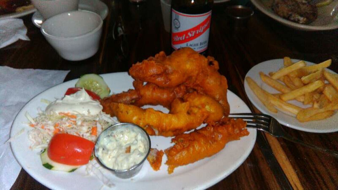 A plate of fish and chips with coleslaw, a small salad, and a cup of sauce.