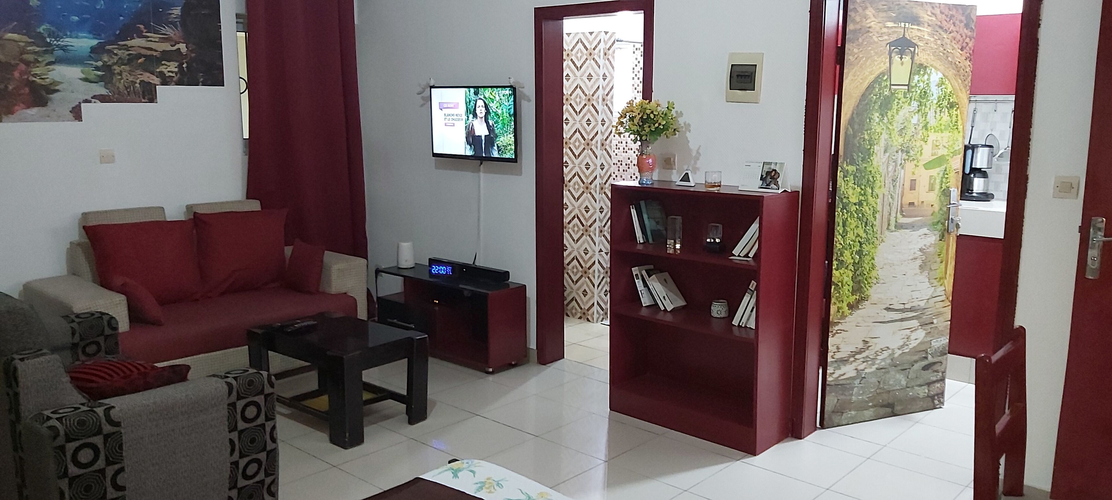 A living room with a red sofa, a coffee table, a bookshelf, and a TV mounted on the wall.