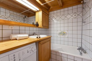Een badkamer met een houten wastafelmeubel, een witte wasbak en een bad.