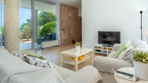 Un salon moderne doté d’un grand téléviseur, de sièges confortables, d’une table basse et offrant une vue sur l’extérieur.
