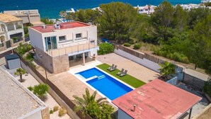 Une maison moderne à deux étages, dotée d’une piscine, entourée de verdure et offrant une vue sur la mer.