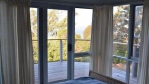 A room with a bed, large sliding glass doors leading to a balcony with a view of trees. - 60 Karbeethong Avenue, Mallacoota (Mallacoota)