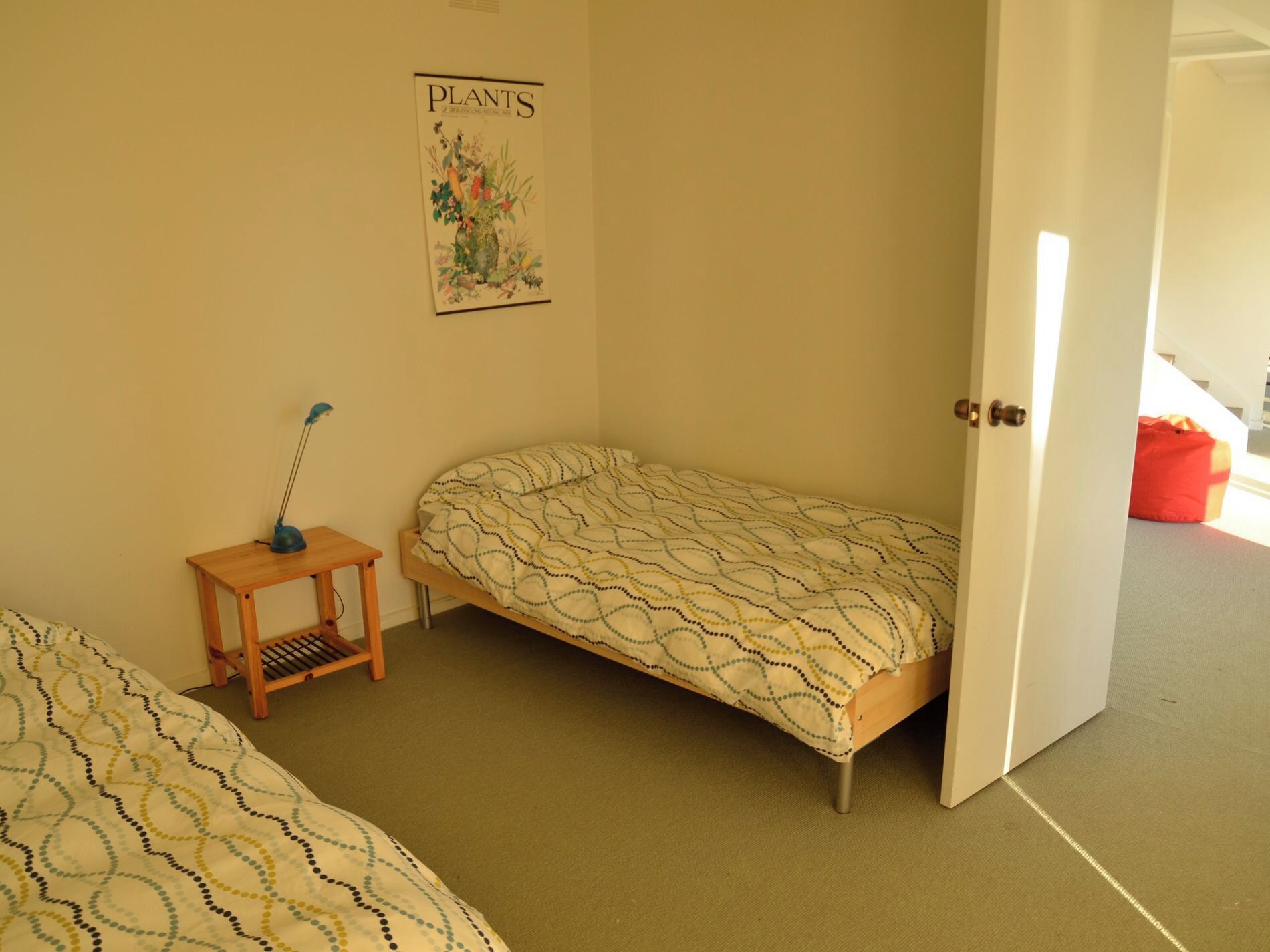 A small, single-bed room with a patterned bedspread, a small wooden table with a lamp, and a poster on the wall.