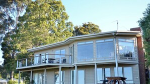 A two-story house with a balcony, large windows, and a picnic table in the front yard. - 60 Karbeethong Avenue, Mallacoota (Mallacoota)