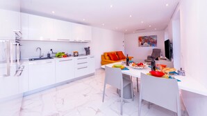 A modern kitchen with white cabinets, a dining table with chairs, and a sofa in the background. - Yellow view apartment - Ronco S/Ascona, Ronco sopra Ascona, Switzerland (Ronco sopra Ascona)