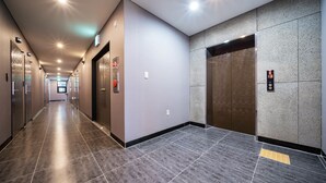 Un pasillo moderno de hotel con un largo acceso, ascensores y una guía táctil en el suelo.
