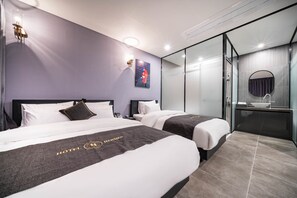 Habitación de hotel con dos camas, zona de ducha con vidrio y un baño pequeño con lavabo y espejo.