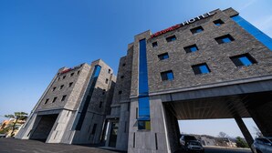 Un hotel moderno con un llamativo letrero que dice 'Hermes Hotel', que presenta un diseño arquitectónico único con una banda azul central y múltiples ventanales.