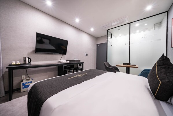 Una habitación de hotel moderna con una cama grande, un escritorio con televisor de pantalla plana, una silla y un muro divisorio de vidrio.