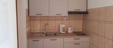A compact kitchen with a sink, two cabinets, a coffee maker, and a trash bin.