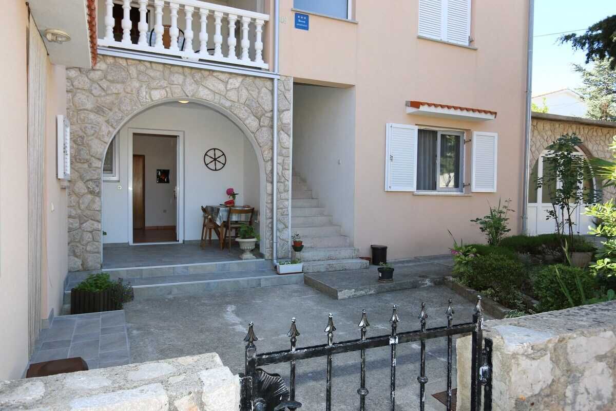 A two-story building with a stone facade, a balcony, and a staircase leading to the entrance.