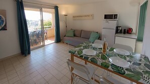 A cozy living area with a sofa, a dining table set for two, a kitchen with a microwave, and a sliding glass door leading to a balcony. - Résidence Les Sangliers by Interhome (Saint-Raphaël)