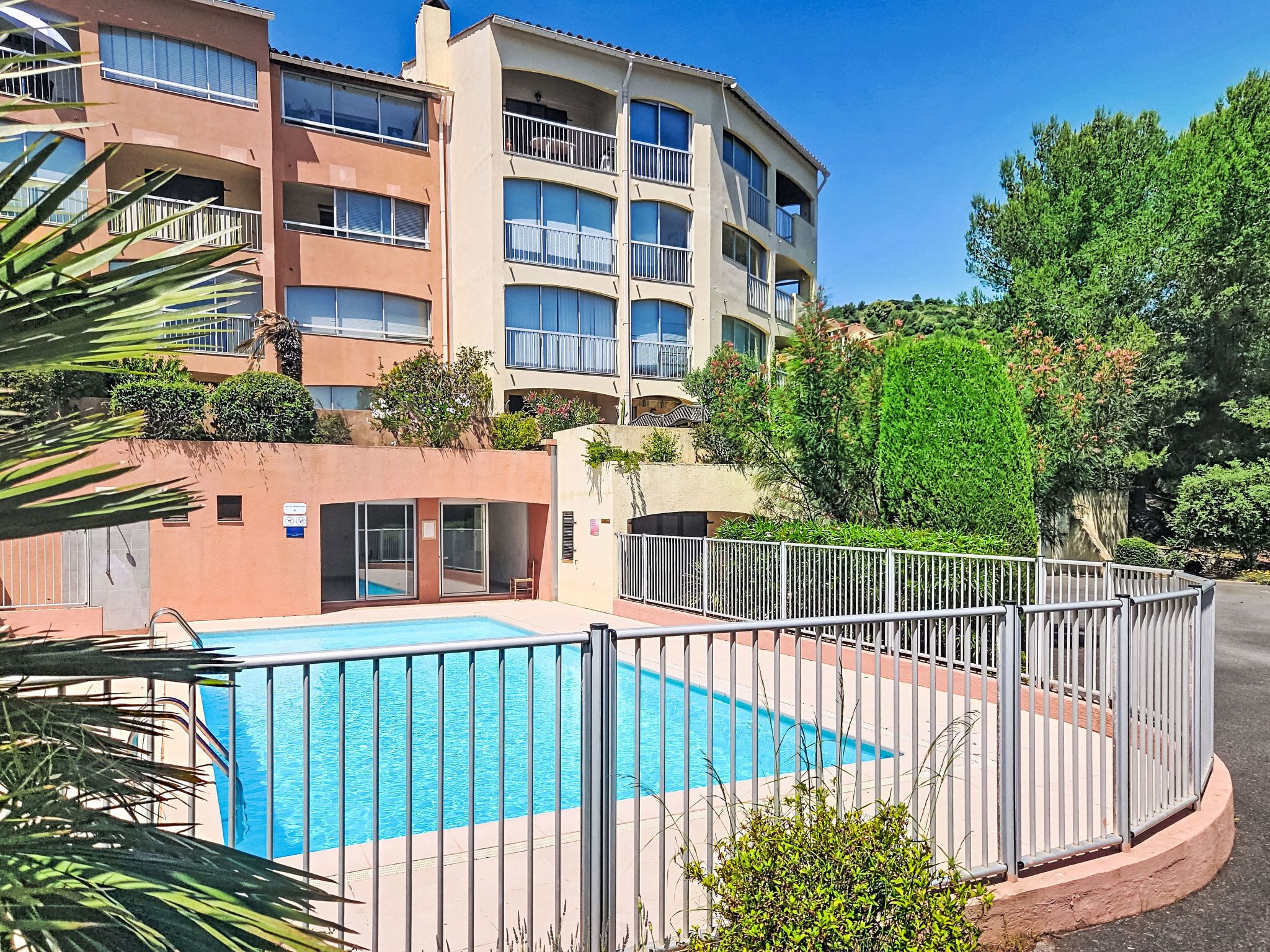 A multi-story residential building with balconies, a swimming pool, and surrounding greenery.