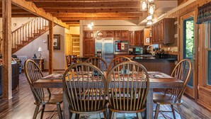 A wooden interior with a dining table and chairs, a kitchen with wooden cabinets, and a staircase.