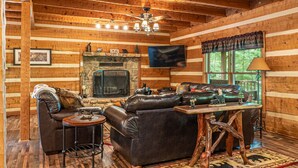 A log cabin interior with a fireplace, leather furniture, and a television.