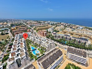 An aerial view of a coastal city with a prominent hotel featuring a rooftop pool and a large red location marker.