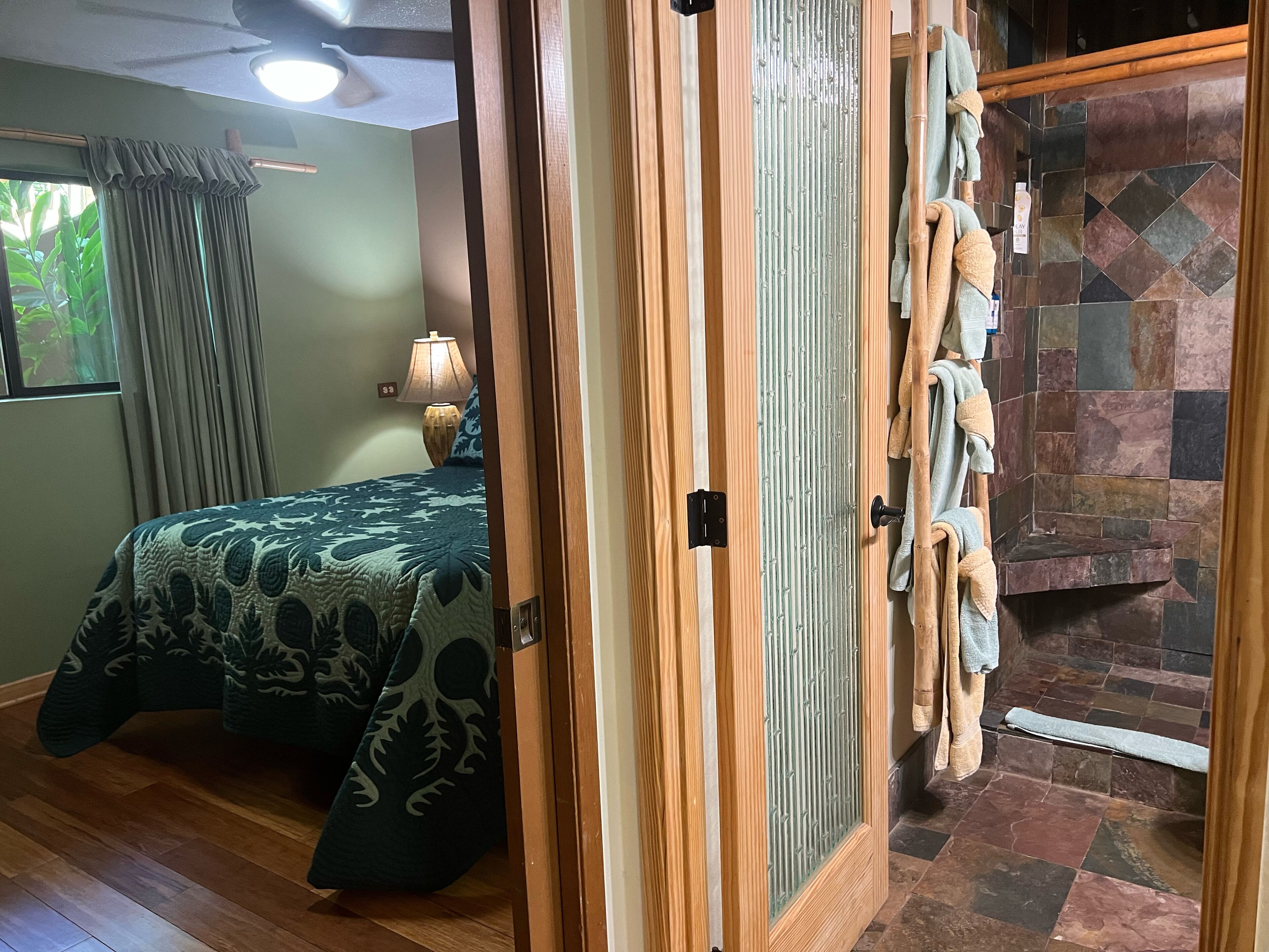 Una habitación con una cama, una puerta de madera, una lámpara y una pared de piedra.