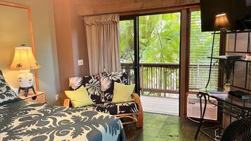 A hotel room with a bed, a sofa, a TV, a lamp, and a view of greenery outside.