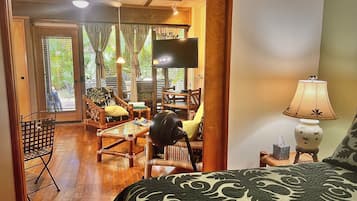 Um quarto com cama, televisão, mesa, cadeiras e ventilador.