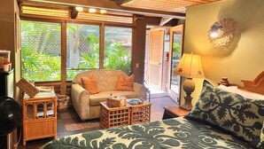 A cozy room with a bed, a sofa, a small table, and a fan. There is a window with blinds, a door, and a wall-mounted lamp. - Maui What A Wonderful World B and B Hawaii  (Kihei)