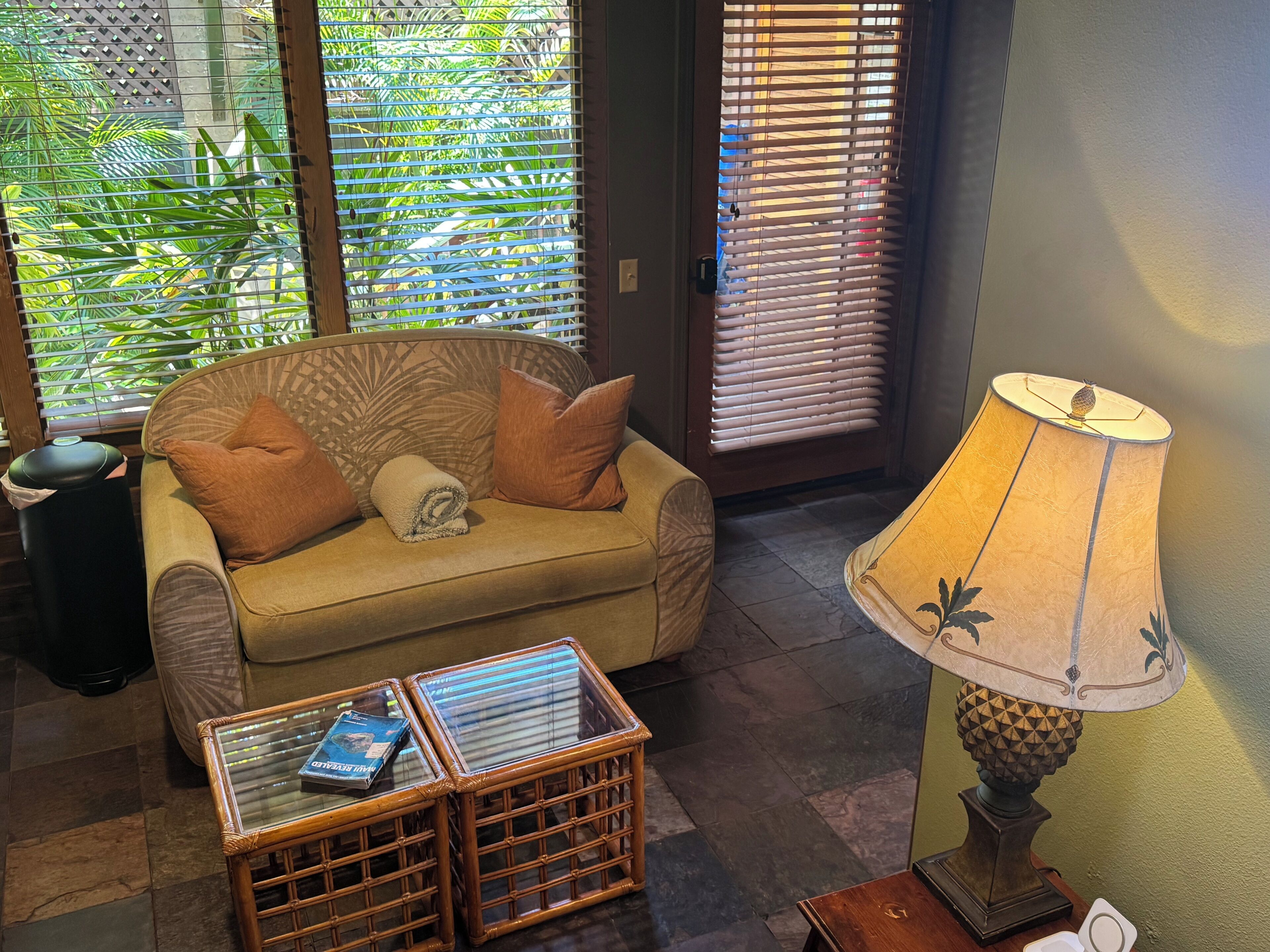 A room with a sofa, a glass-top coffee table with books, a lamp, and a door with blinds.