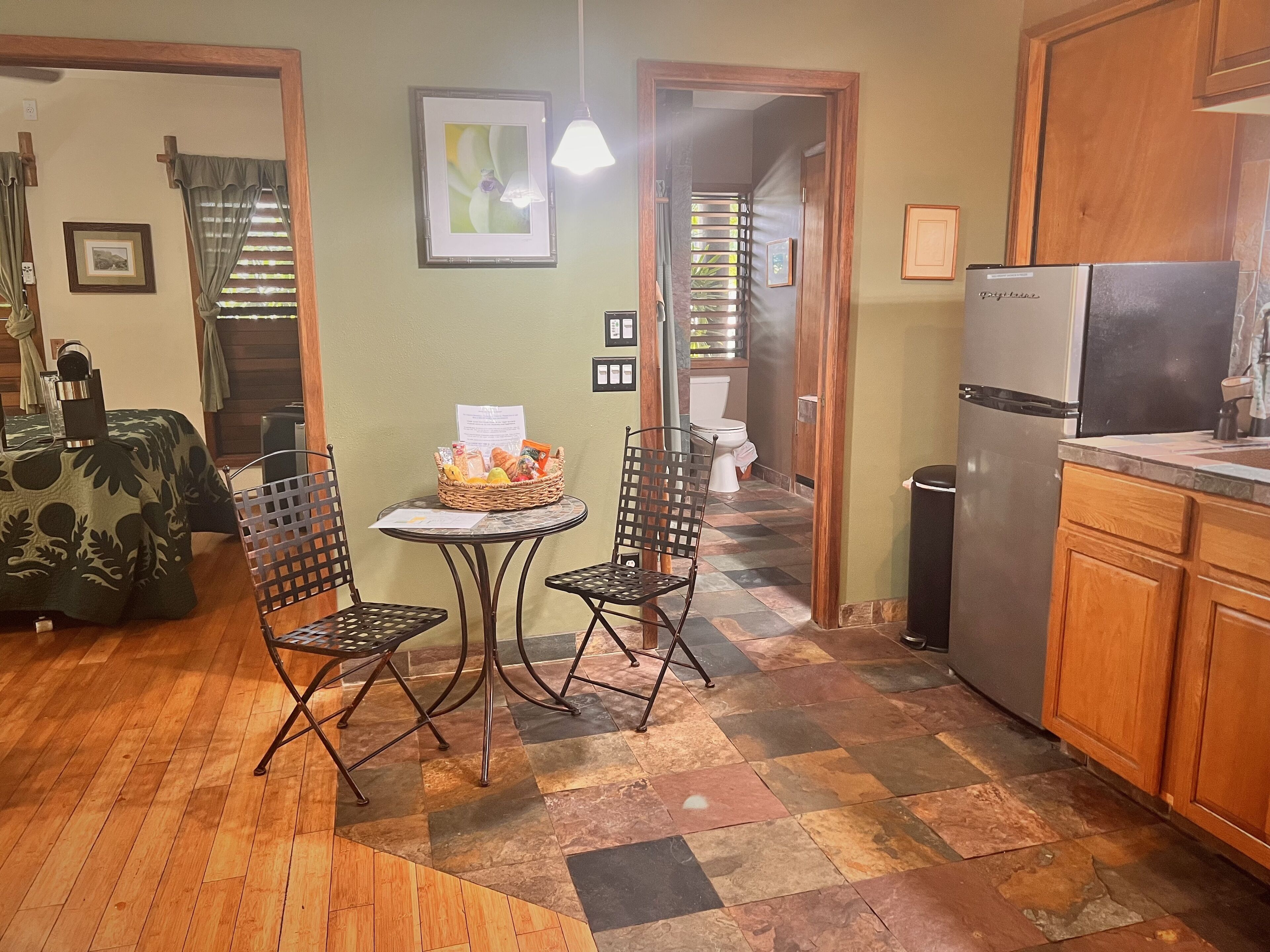 A compact kitchen with a refrigerator, a dining table with chairs, and a small window with curtains.