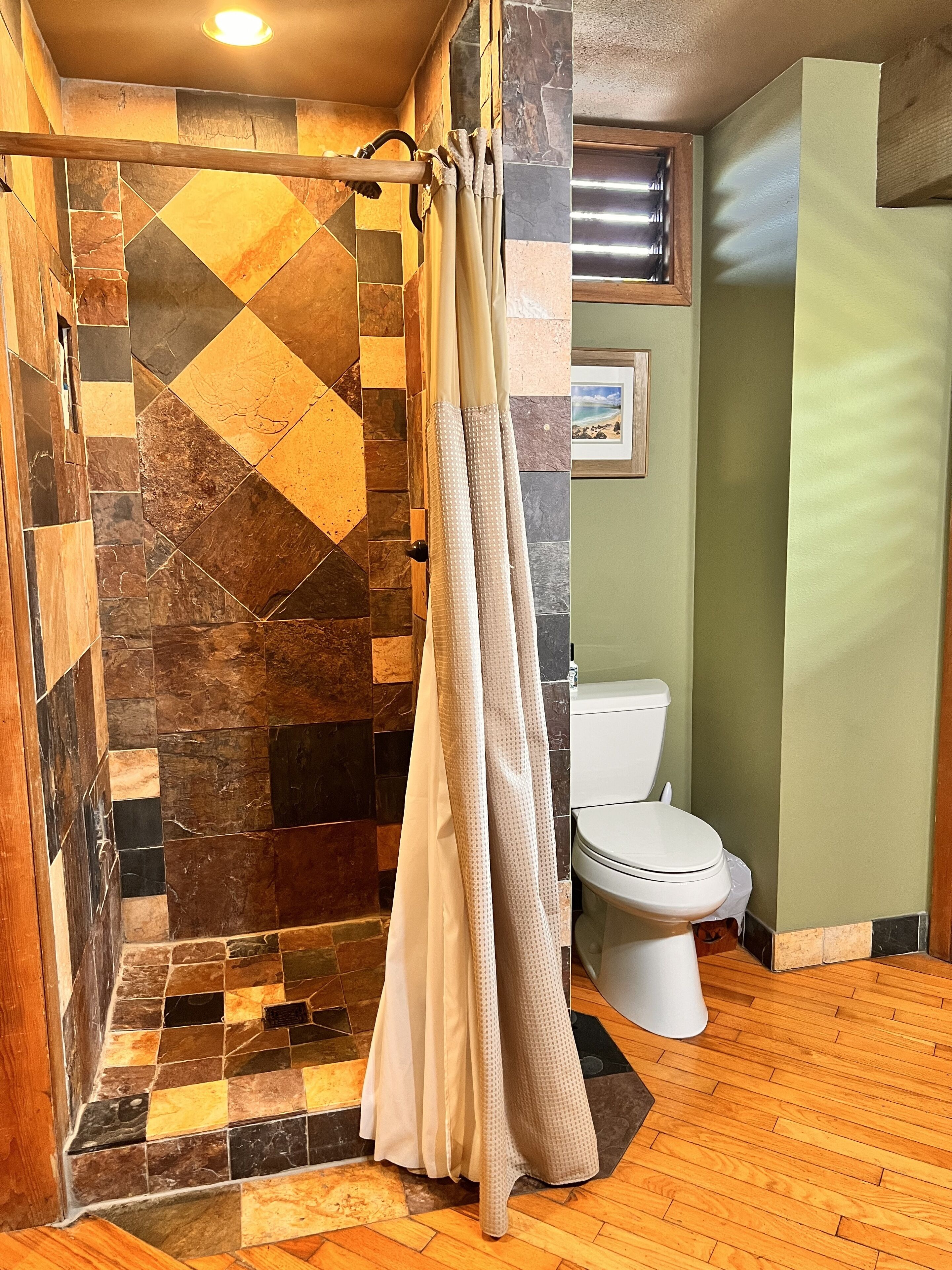 Bagno con zona doccia caratterizzata da una parete in mosaico, un water e un pavimento in legno.
