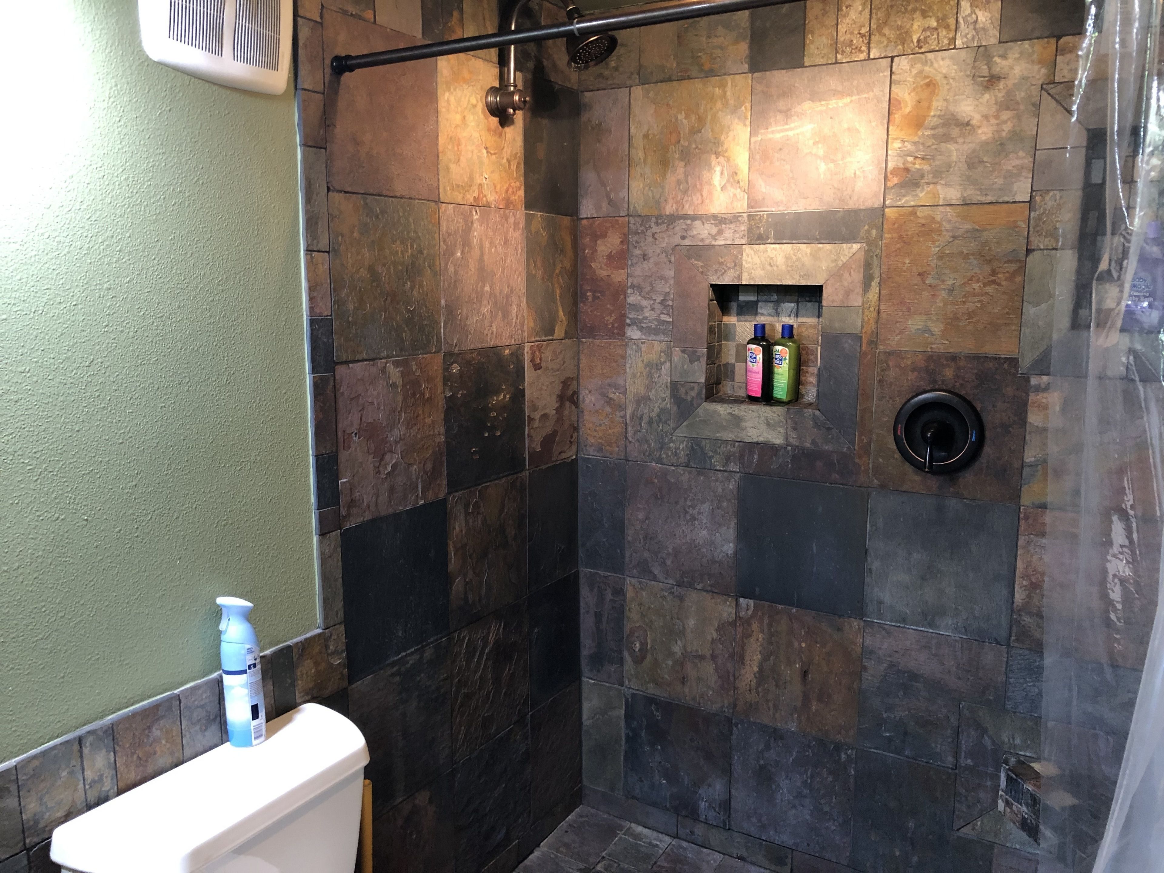 A bathroom with a stone shower wall, a toilet, and a shelf with toiletries.