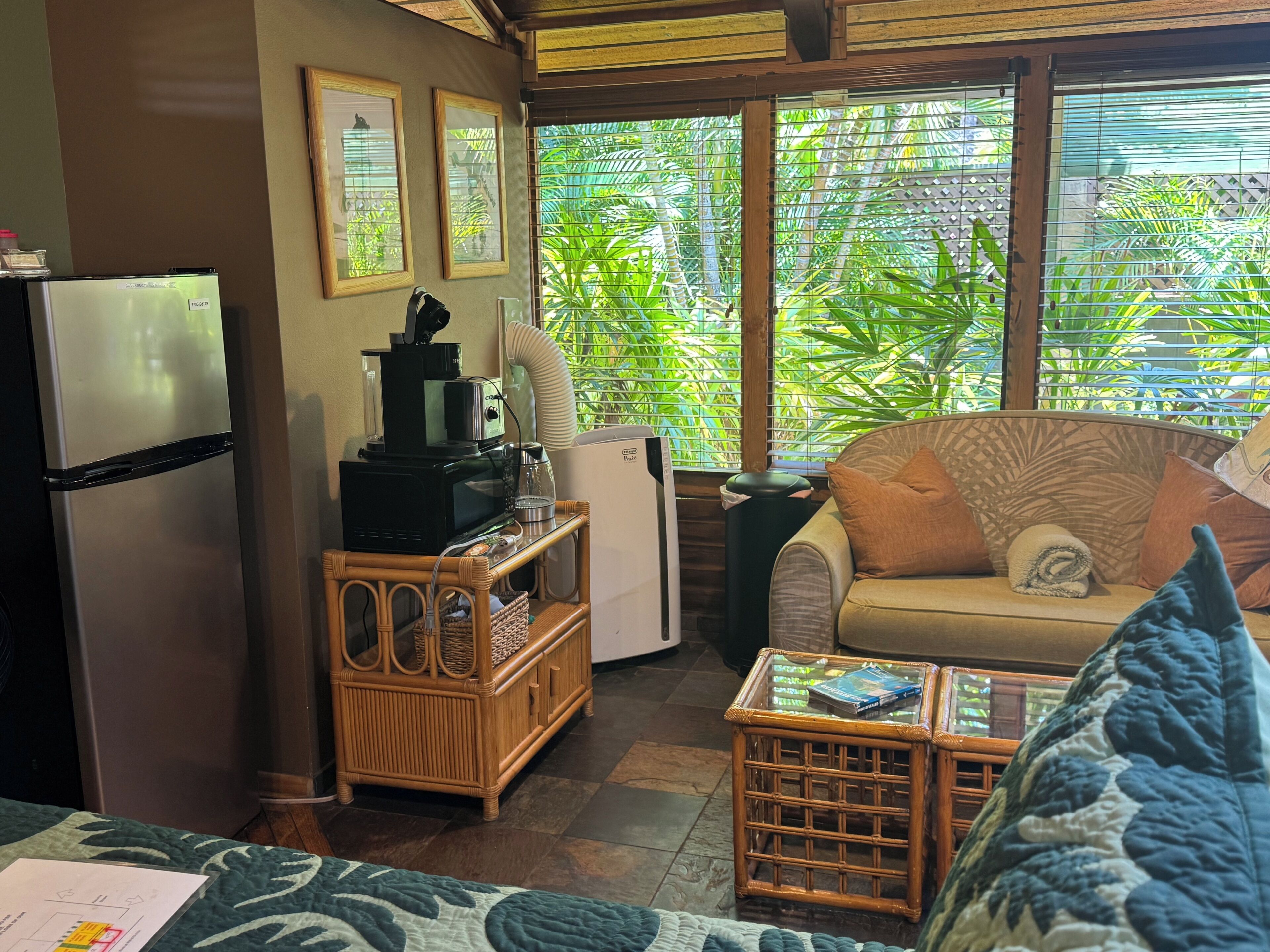 A compact living space with a kitchenette, a sofa, a coffee table, and a view of lush greenery through the windows.