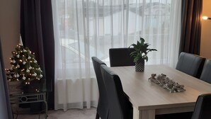 Un comedor moderno con una mesa de madera, sillas negras, un árbol de Navidad y un amplio ventanal con cortinas traslúcidas.