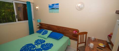 A bedroom with a bed, a wooden headboard, a bedside table with a lamp, a chair, and a small table with a bowl and a cup.