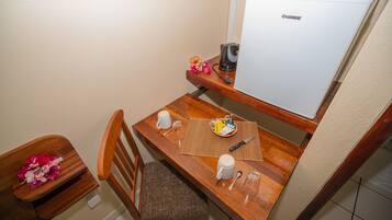 A compact kitchenette with a coffee maker, a small refrigerator, and a dining area with a chair and table.