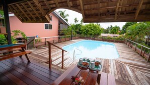 Una terraza de madera con piscina, mesa de picnic y sillas de descanso.