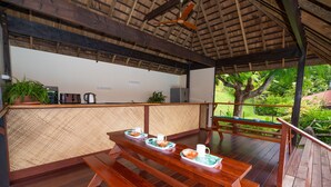 Una terraza de madera con una mesa dispuesta para dos personas, un ventilador de techo y vistas a la vegetación.