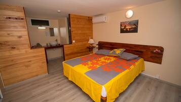 A bedroom with a wooden headboard, a bed with a yellow and gray floral bedspread, a nightstand with a lamp, and a wall-mounted TV.