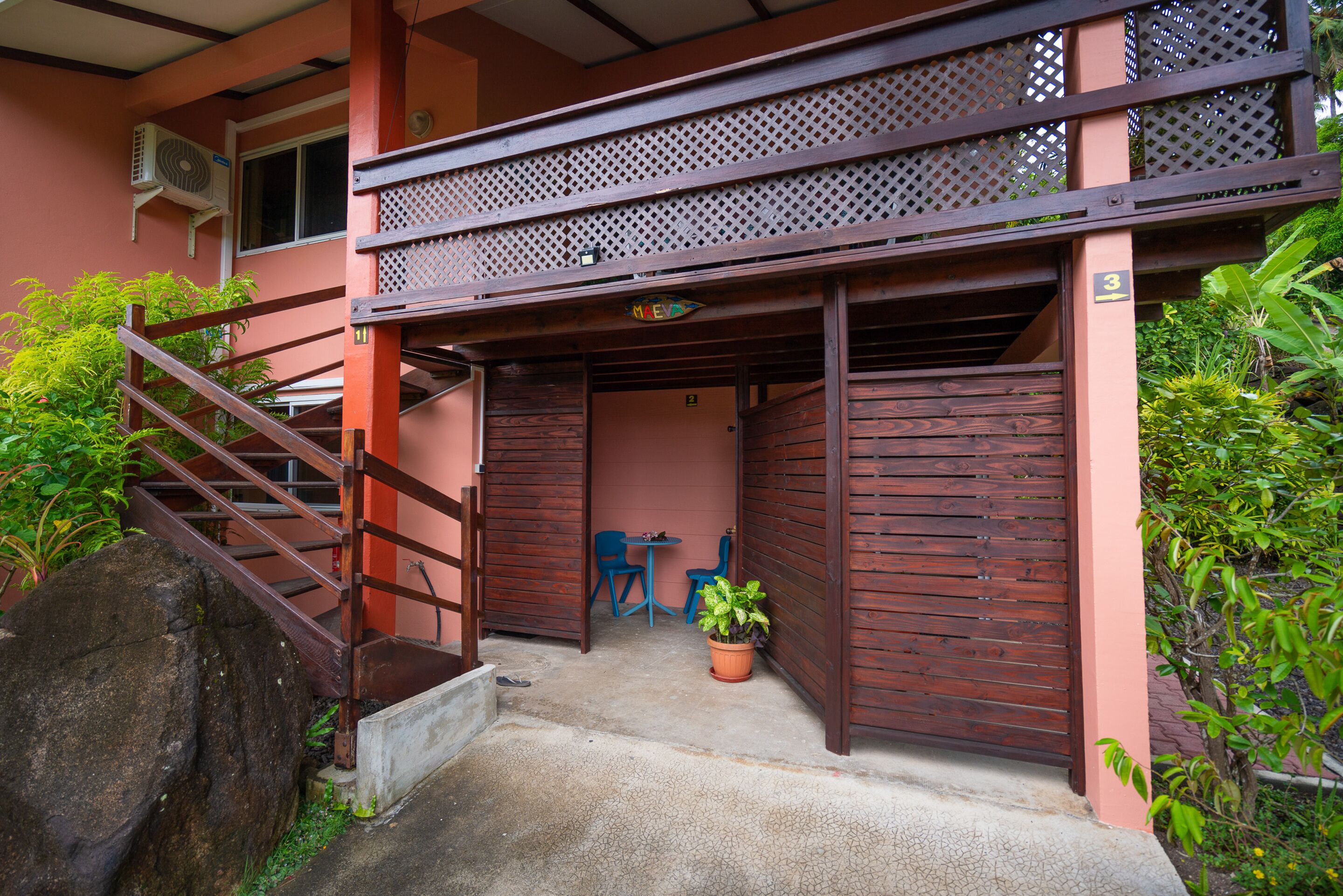 Un edificio con una escalera de madera, una pequeña mesa con sillas y una planta en maceta.