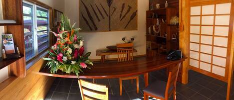 A traditional Japanese-style room with a wooden reception desk, a dining table with chairs, a decorative flower arrangement, and a shoji screen.