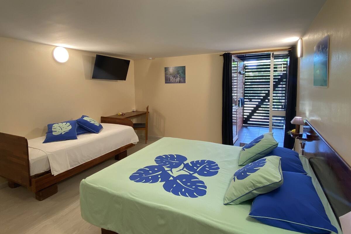 A bedroom with two beds, a TV mounted on the wall, and a window with blinds.