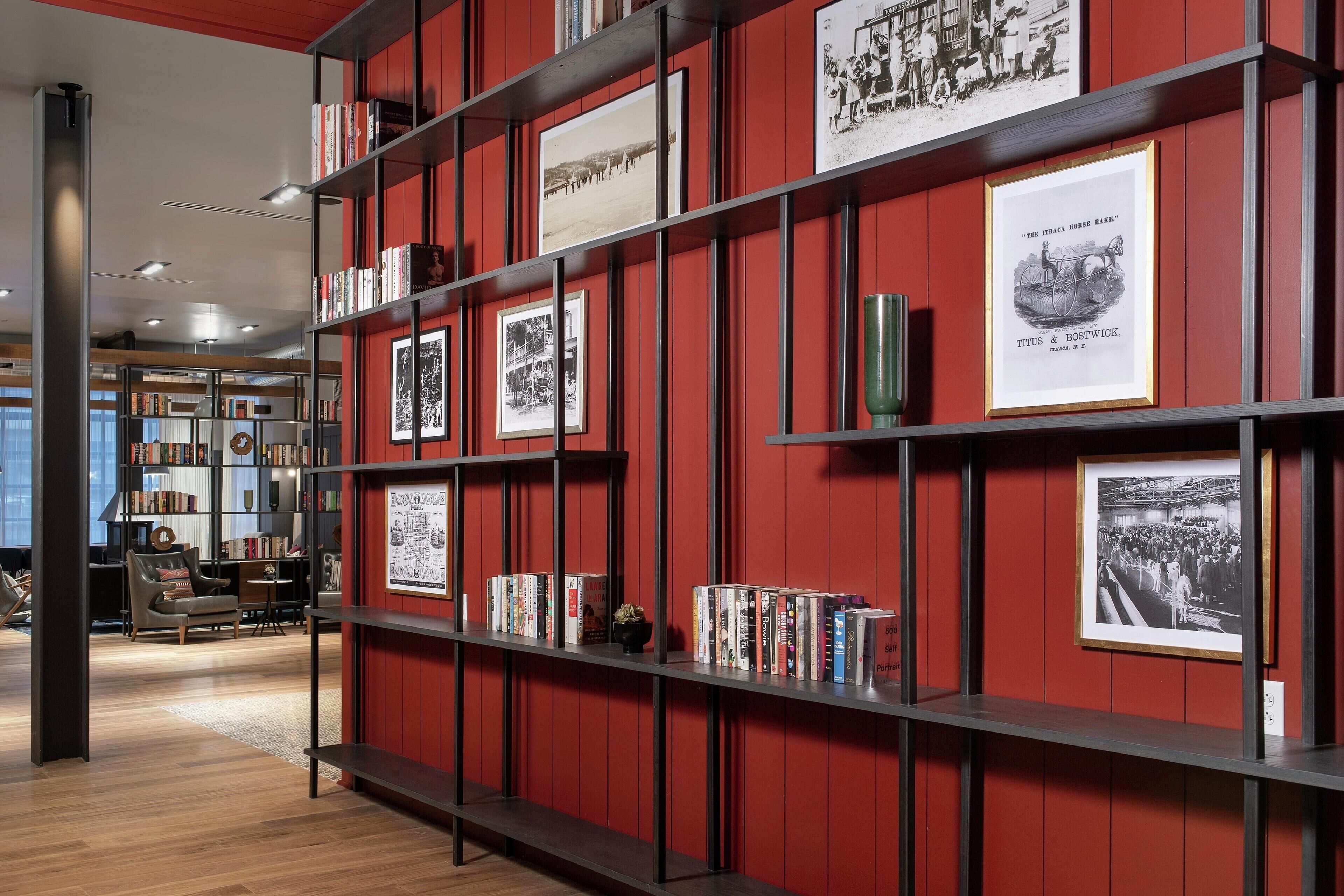 A library with bookshelves, framed pictures, and a red wall.