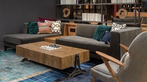 A modern living room with a sectional sofa, a wooden coffee table, and a bookshelf filled with books and decorative items. - Canopy by Hilton Ithaca Downtown (Ithaca)