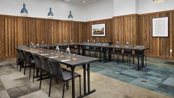 Une salle de conférence avec une longue table, des chaises et des luminaires suspendus.