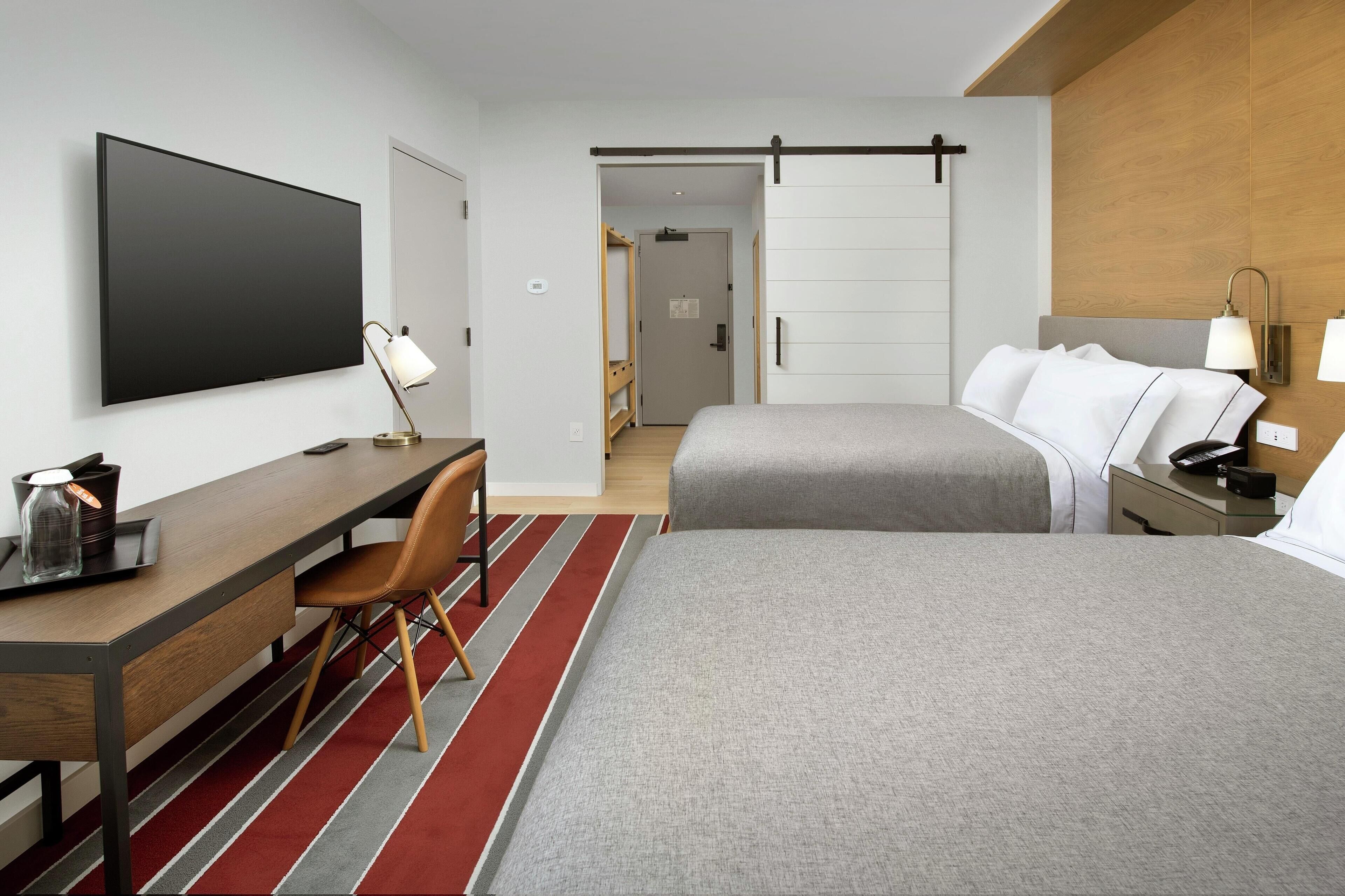 Une chambre d’hôtel comprenant un lit, un bureau avec une chaise, une télévision et une table de chevet avec une lampe.