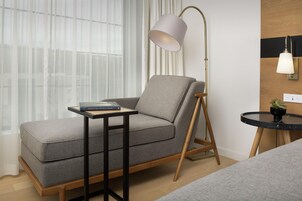 Una sala de estar moderna con un sofá gris, una mesita auxiliar pequeña, una lámpara de pie y una mesita redonda con una planta.
