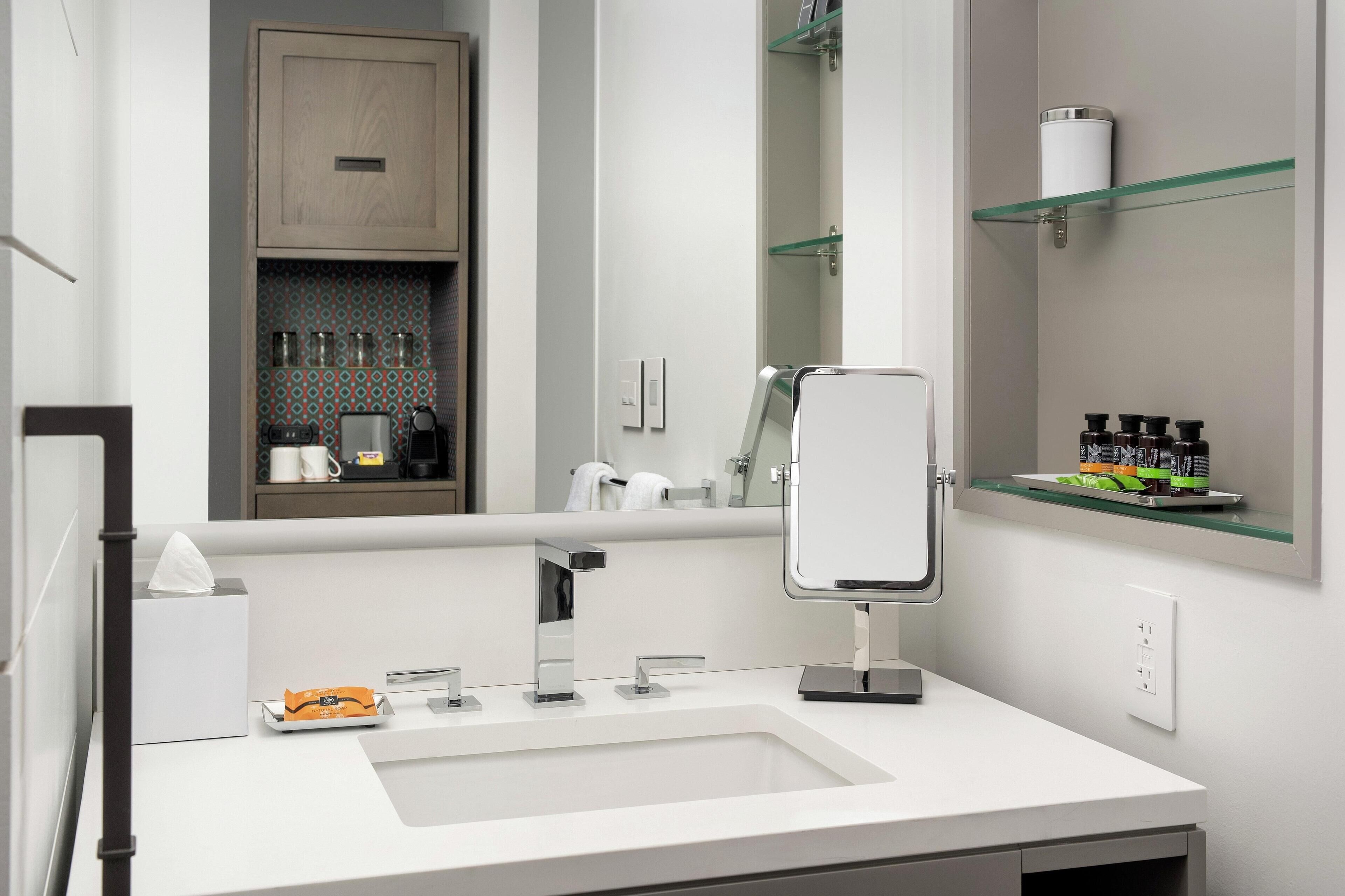 A modern bathroom with a white sink, a mirror, and a cabinet with toiletries.