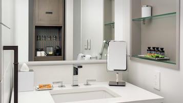 A modern bathroom with a white sink, a mirror, and a cabinet with toiletries.