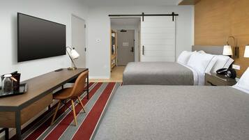 A hotel room with a bed, a desk with a chair, a TV, and a bedside table with a lamp.