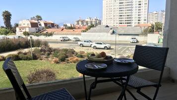 Een balkon met rieten stoelen en een tafel gedekt voor ontbijt, met uitzicht op een parkeerplaats en gebouwen.