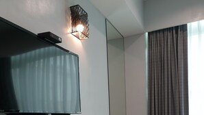 Une chambre d’hôtel avec un bureau en bois, un téléviseur à écran plat fixé au mur, un miroir et une fenêtre avec des rideaux.