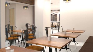 Un espace de restauration moderne avec des tables en bois et des chaises en métal, agrémenté de luminaires suspendus et d’un plafond haut avec des poutres apparentes.